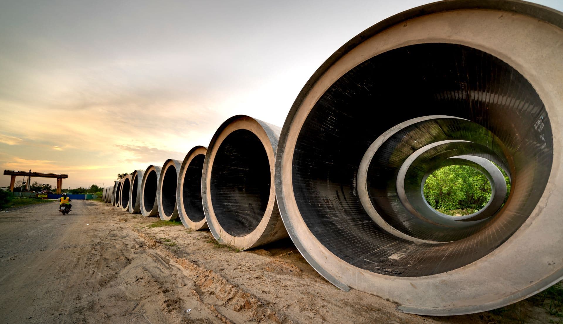Row of large jacking pipes laid out on a site access road at sunset