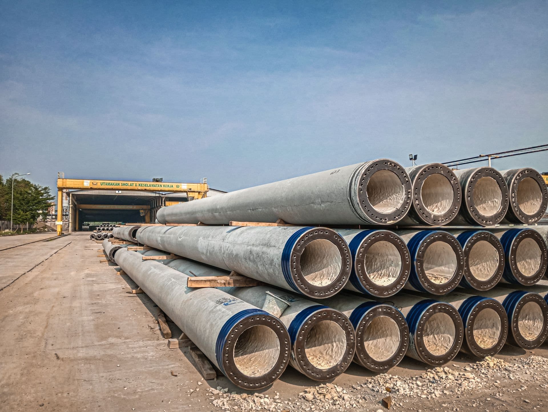 Large-diameter concrete pipes stacked in a plant yard beneath a gantry crane