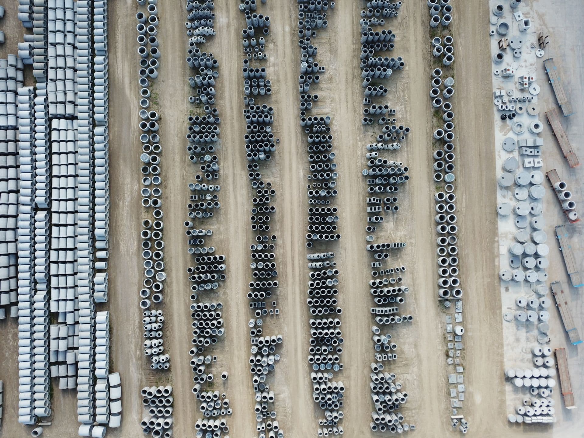 Aerial view of a precast storage yard with rows of concrete pipes, rings and box sections